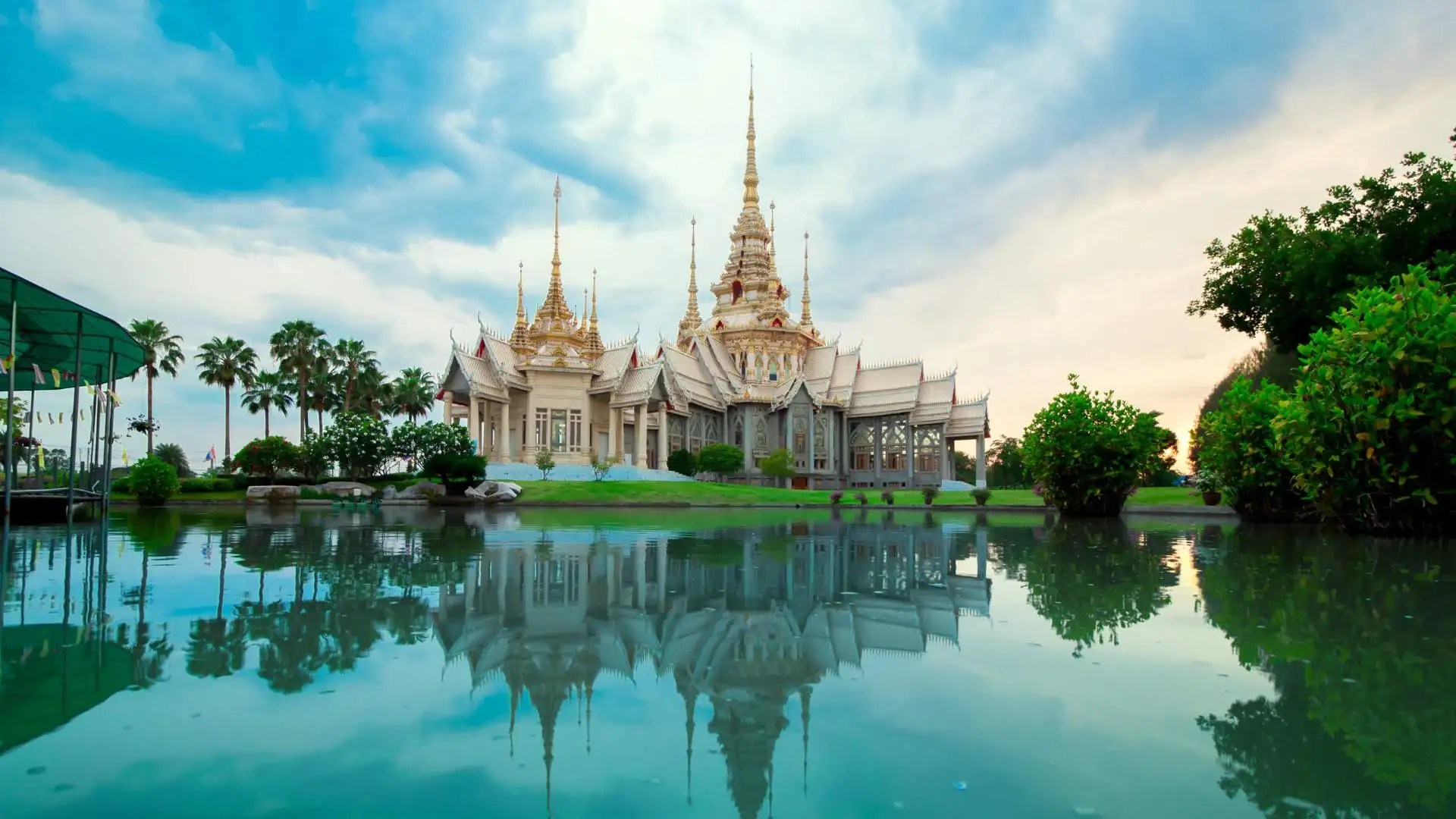 Un temple thaïlandais avec des toits dorés et des flèches, reflété dans l'eau.