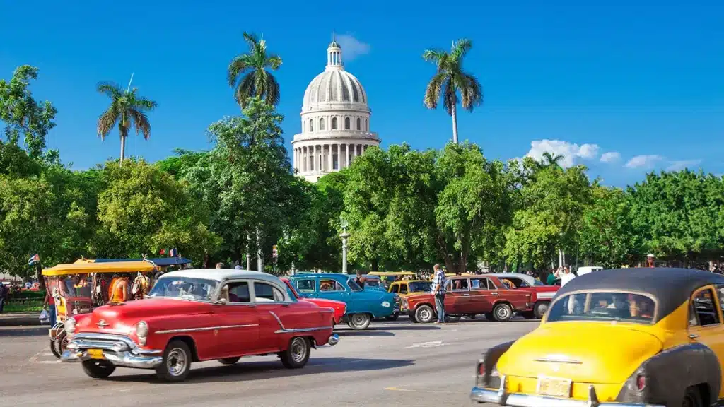 Le majestueux Capitole de La Havane entouré de voitures classiques cubaines et de végétation tropicale. Un passage obligé de tout voyage sur mesure à Cuba, orchestré par notre agence de voyage à Lyon.
