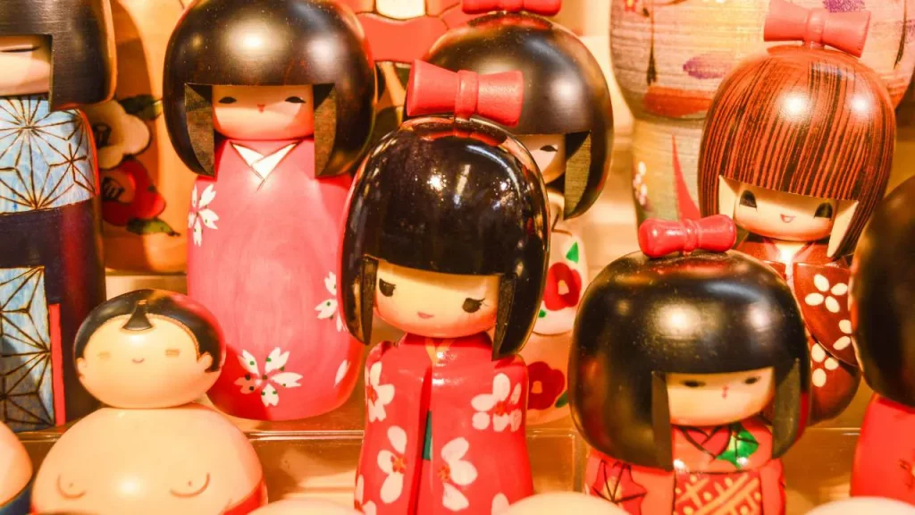 Collection de poupées kokeshi japonaises en bois peint avec des kimonos roses et rouges exposées dans une boutique d'artisanat traditionnel