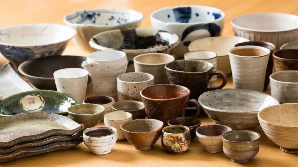 Assortiment de bols, tasses et plats en céramique japonaise aux tons beiges et bruns disposés sur une table en bois