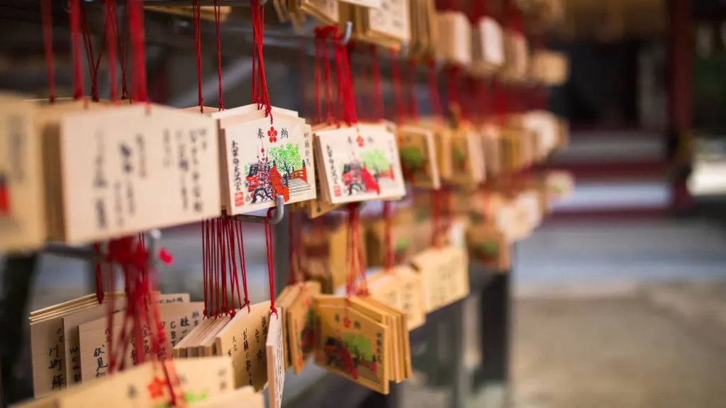 Rangées de plaquettes votives ema en bois suspendues par des cordons rouges dans un sanctuaire japonais avec des inscriptions et dessins colorés