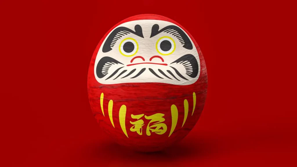 Poupée daruma rouge traditionnelle avec un visage blanc peint, des yeux dorés et des caractères japonais dorés sur fond rouge uni