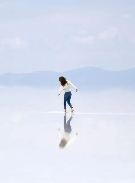Femme marchant sur miroir naturel Salar d'Uyuni Bolivie reflet parfait ciel voyage sur mesure Bolivie