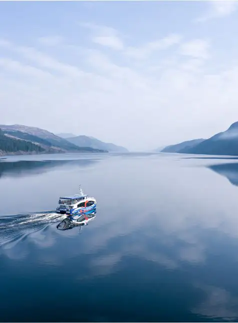 Bateau de croisière naviguant sur loch paisible entouré de montagnes pour voyage sur mesure en Écosse