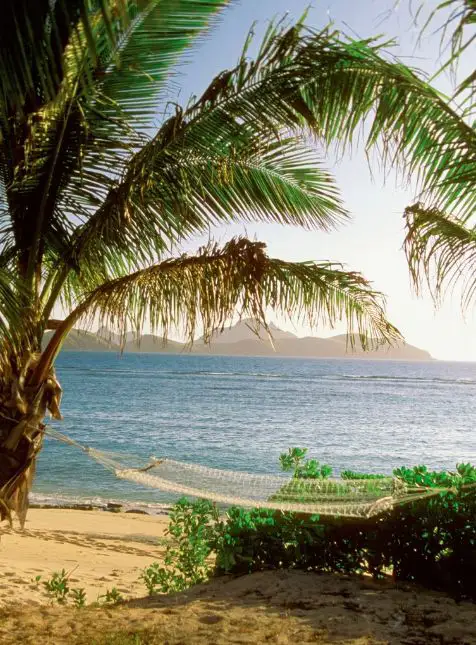 Hamac sous palmier face au lagon turquoise et montagnes aux Fidji pour voyage sur mesure Fidji relaxation luxe