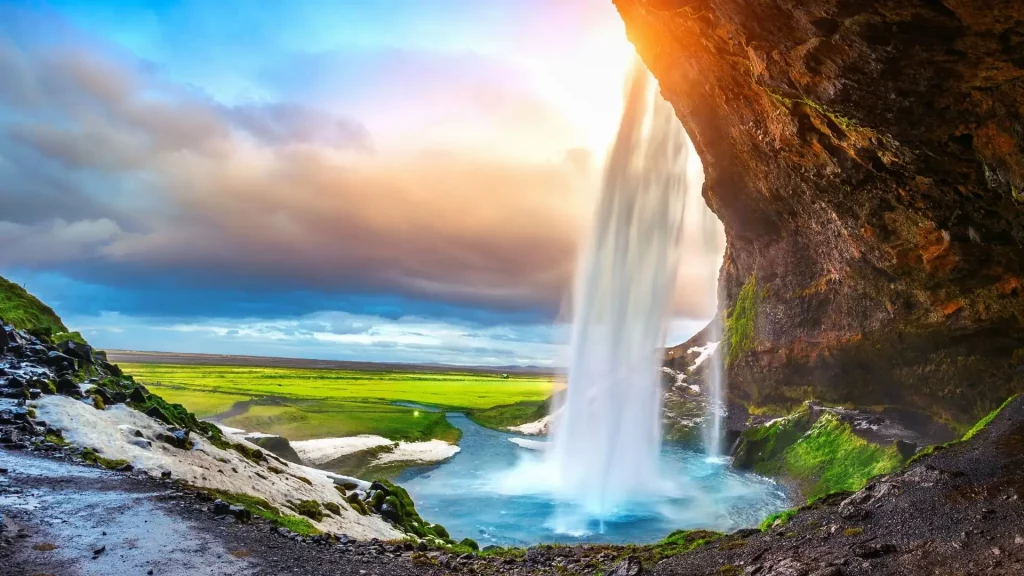 Cascade Seljalandsfoss vue de l'intérieur avec plaines vertes et ciel dramatique - voyage sur mesure en Islande avec Les Sens du Voyage