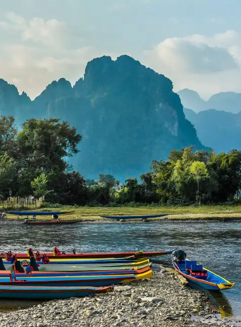 Pirogues multicolores au bord de la rivière avec pitons karstiques à Vang Vieng pendant un voyage sur mesure au Laos