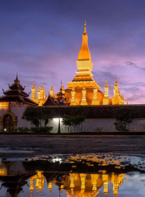 Stupa doré Pha That Luang illuminé au crépuscule avec reflet dans l'eau lors d'un voyage sur mesure au Laos