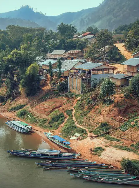 Village traditionnel laotien avec maisons colorées et bateaux sur le Mékong pendant un voyage sur mesure au Laos