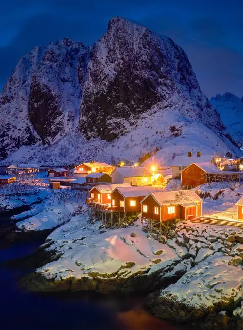 Village de pêcheurs illuminé à l'heure bleue dans les îles Lofoten pour un voyage sur mesure en Norvège avec montagnes enneigées