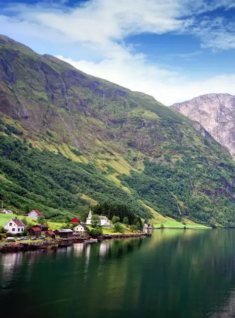Village norvégien traditionnel au bord d'un fjord avec église et montagnes vertes pour un voyage sur mesure en Norvège