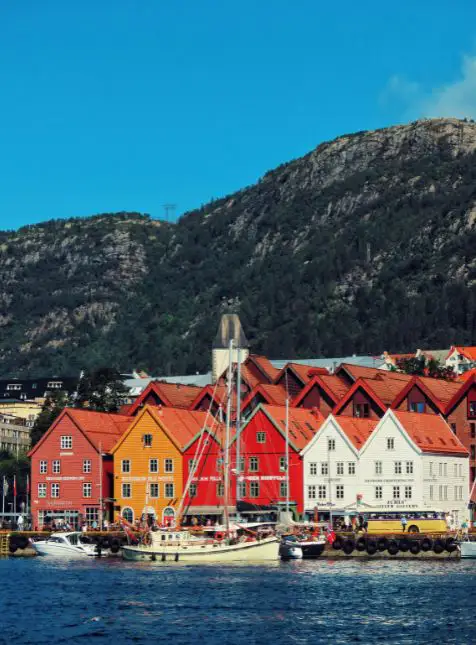 Façades colorées du port de Bergen avec bateaux et montagnes pour un voyage sur mesure en Norvège à Bryggen