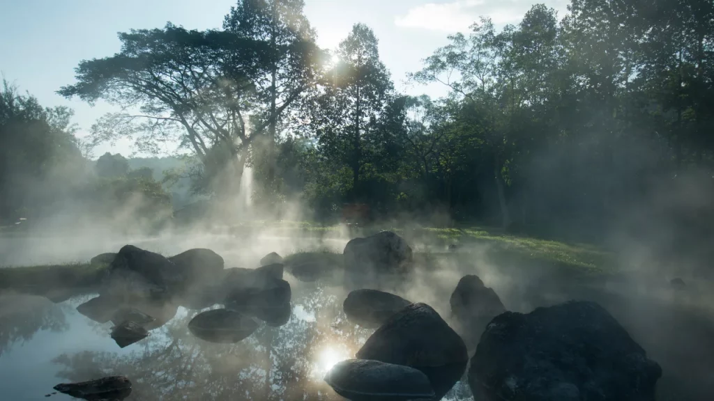 Sources chaudes naturelles dans une forêt brumeuse avec rochers et rayons de soleil lors d'un voyage sur mesure en Thaïlande