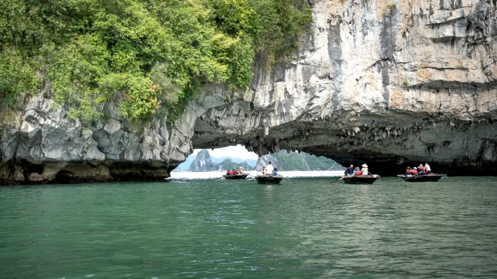 ques traversant une arche naturelle de calcaire pour accéder à une lagune secrète de la baie d'Halong lors d'un voyage sur mesure au Vietnam