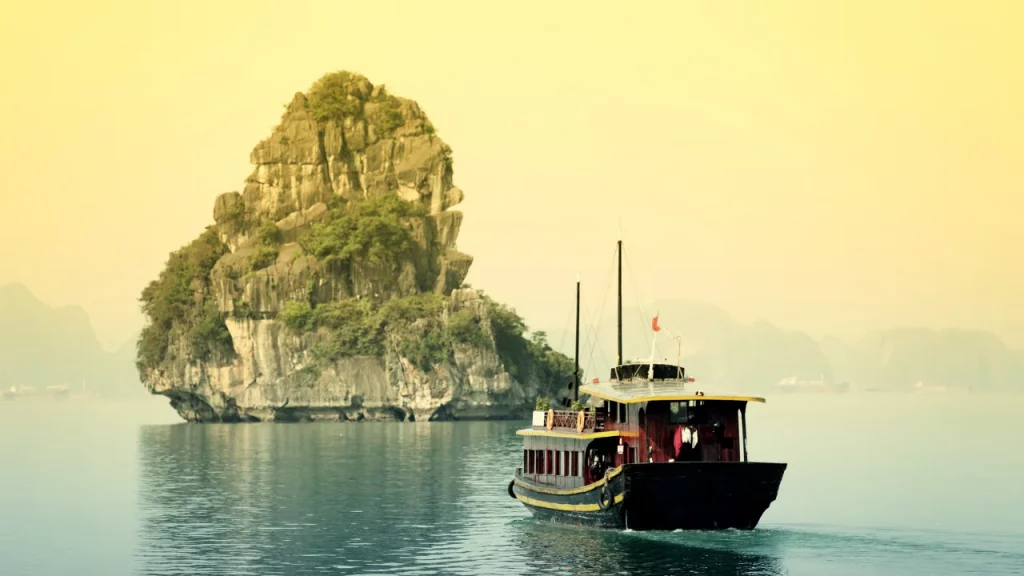 Jonque solitaire naviguant dans la brume face à un piton calcaire de la baie d'Halong lors d'un voyage sur mesure au Vietnam