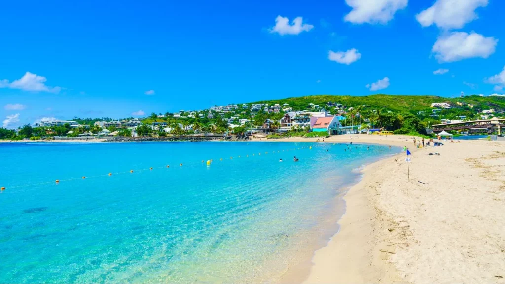 Plage de sable blanc avec eaux turquoise et village en bord de mer lors d'un voyage sur mesure à La Réunion