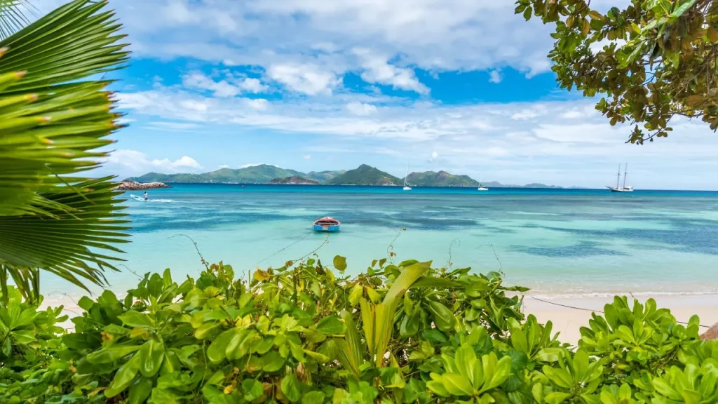 Plage tropicale avec végétation, voiliers et île en arrière-plan lors d'un voyage sur mesure à La Réunion