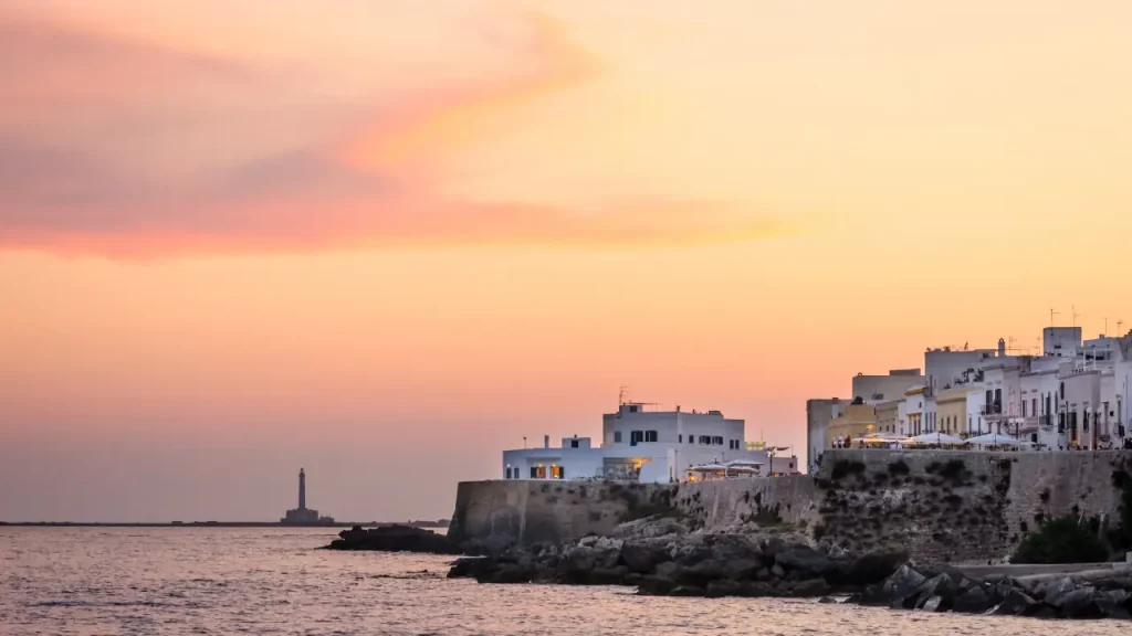 Remparts et maisons blanches de Gallipoli au coucher du soleil rose avec phare en mer lors d'un voyage sur mesure en Italie