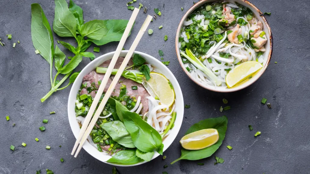 Deux bols de pho vietnamien avec herbes fraîches et baguettes, gastronomie traditionnelle lors d'un voyage sur mesure au Vietnam