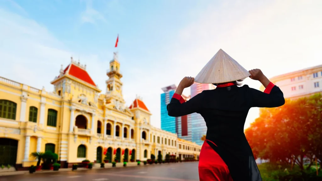 Femme en tenue traditionnelle vietnamienne devant l'Hôtel de Ville de Hô Chi Minh-Ville lors d'un voyage sur mesure au Vietnam