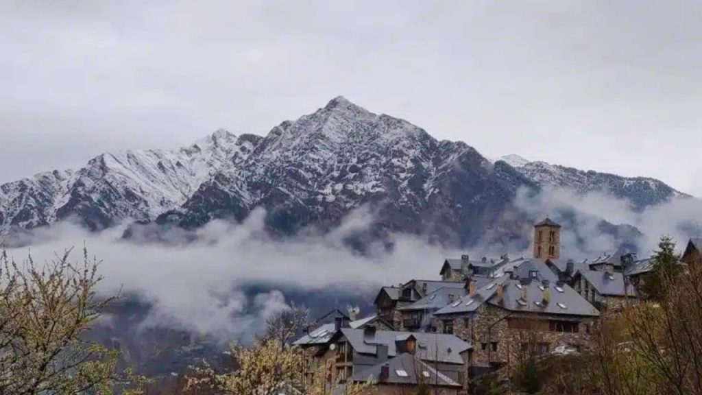 Village de montagne pyrénéen sous sommets enneigés et nuages