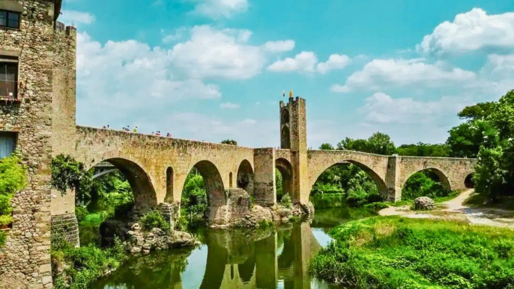 Pont médiéval en pierre avec tour sur rivière verdoyante