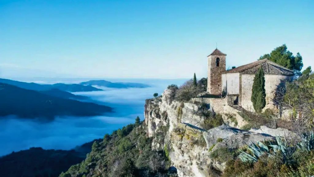 Église romane perchée sur falaise rocheuse au-dessus des nuages