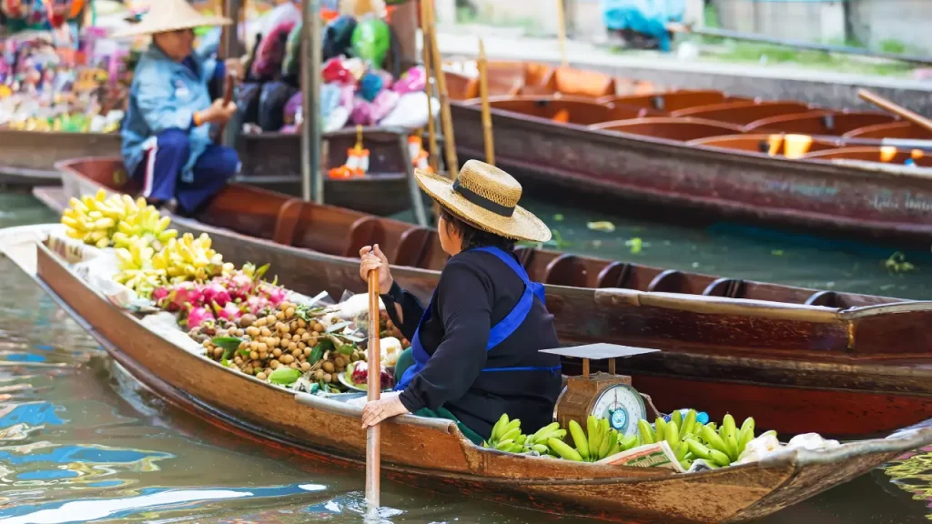 Vendeur sur barque au marché flottant thaïlandais avec fruits